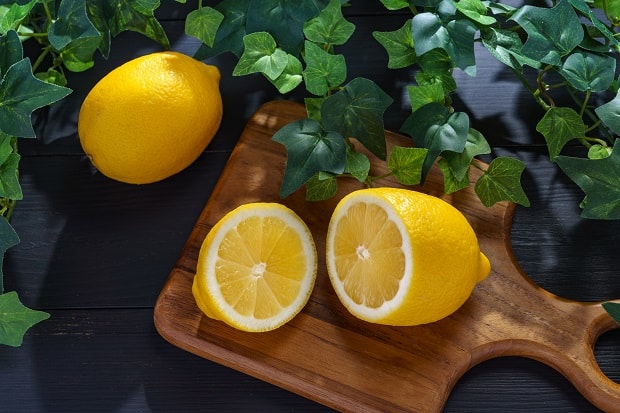 половинки лимона на разделочной доске, рядом целый лимон на столе с зеленой листвой